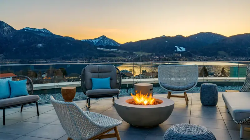 A-ROSA Tegernsee Un tavolo e delle sedie su una terrazza affacciata su uno specchio d'acqua.