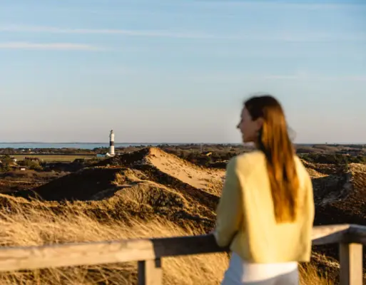 Frühbucher Eine Frau steht an einem Zaun und blickt auf einen Leuchtturm.