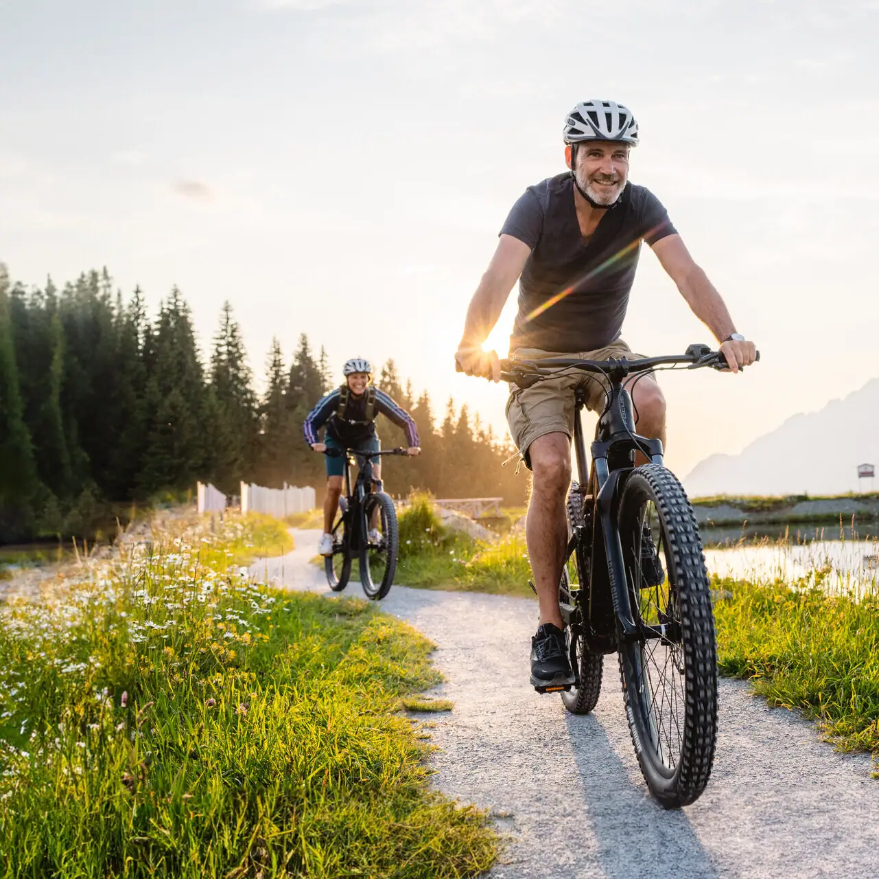 Un uomo in bicicletta su un sentiero con un lago e montagne sullo sfondo.