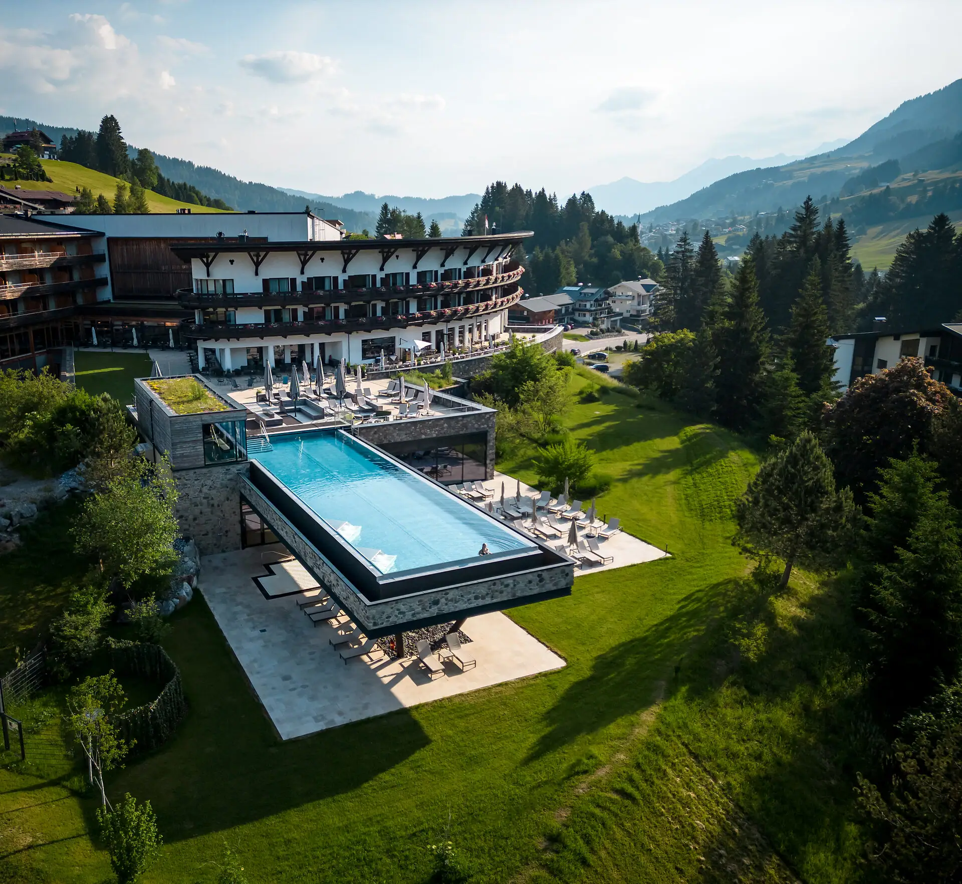 A-ROSA Ifen Hotel Kleinwalsertal Una piscina all'aperto in un hotel, circondata da alberi e da un cielo limpido.