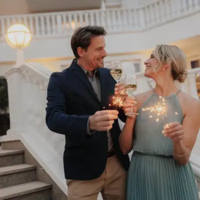 Pacchetti di Capodanno Un uomo e una donna tengono in mano dei bicchieri da vino e sorridono.